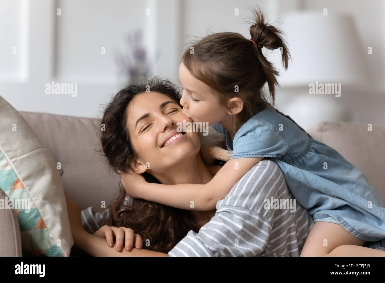 Little daughter gently cuddles kisses mother on cheek showing love
