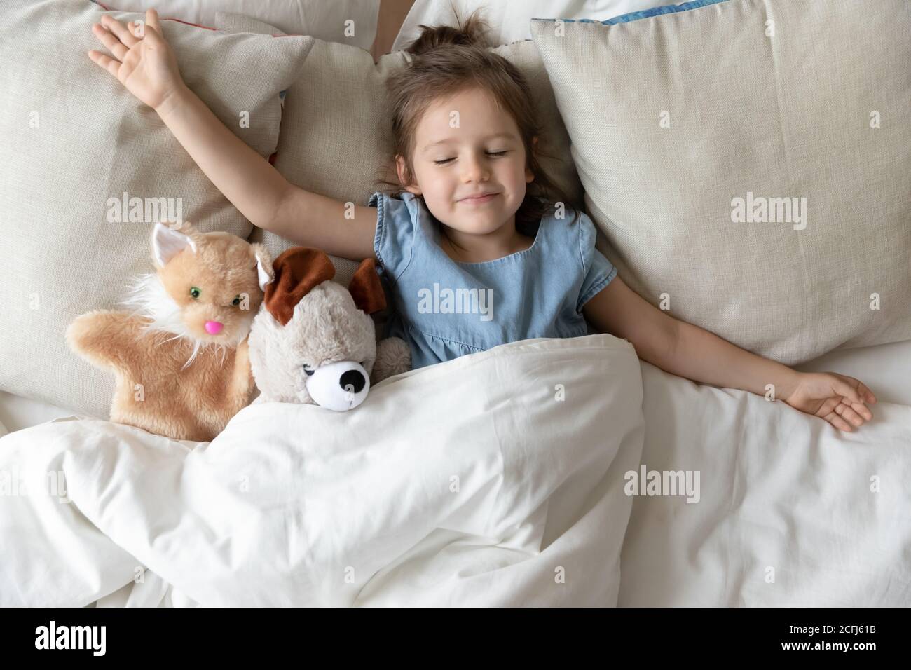 Little girl sleeping in bed with fluffy animal toys Stock Photo