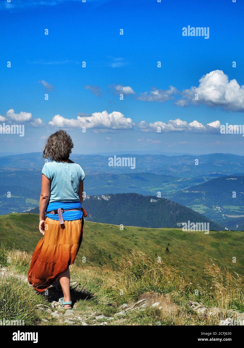 LITTLE FATRA, SLOVAKIA - 08/03/2018: Senior caucasian hippie woman in long orange skirt hiking in Little Fatra National Park and looking at horizon. Stock Photo