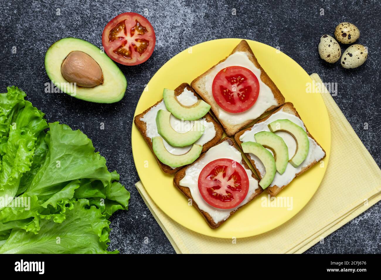 Avocado and tomato sandwich on a yellow plate. Lettuce leaf and quail egg on a dark board. Vegetarian food, dieting nutrition concept, still life. Toa Stock Photo