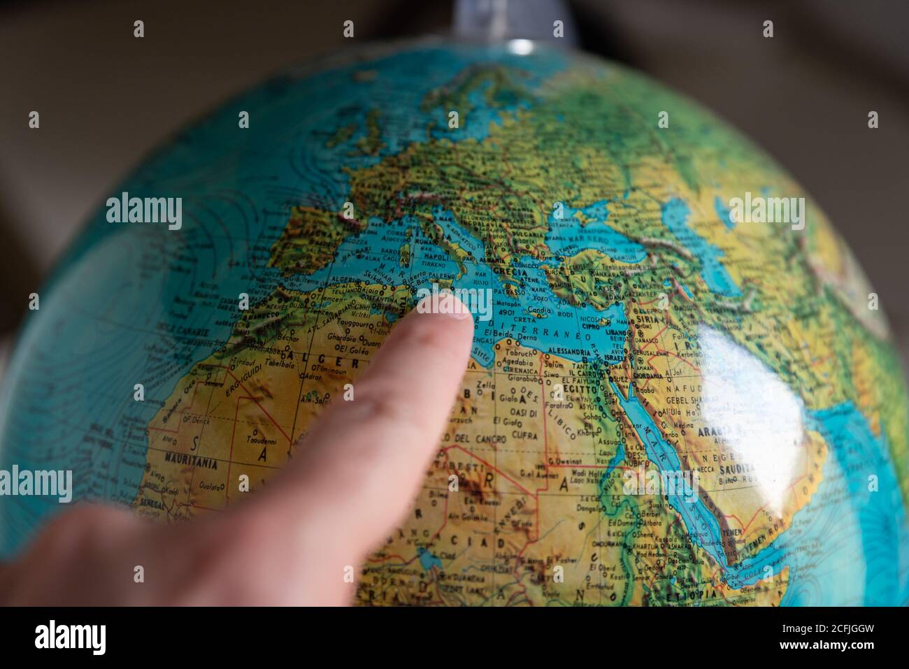 Index finger indicates Sicily on the globe, close up, blurred at the desired edges Stock Photo