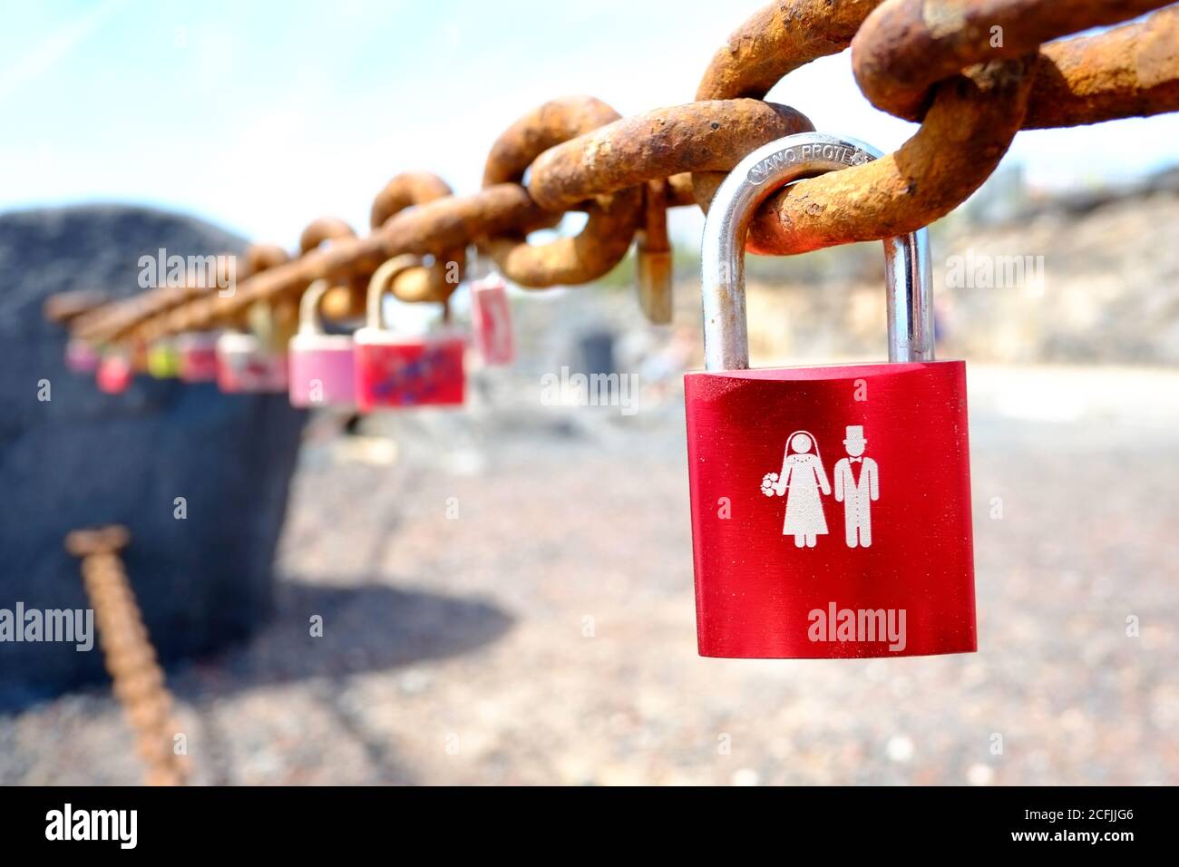 A red padlock, or love lock, attached to an old chain depicting a bride and groom Stock Photo