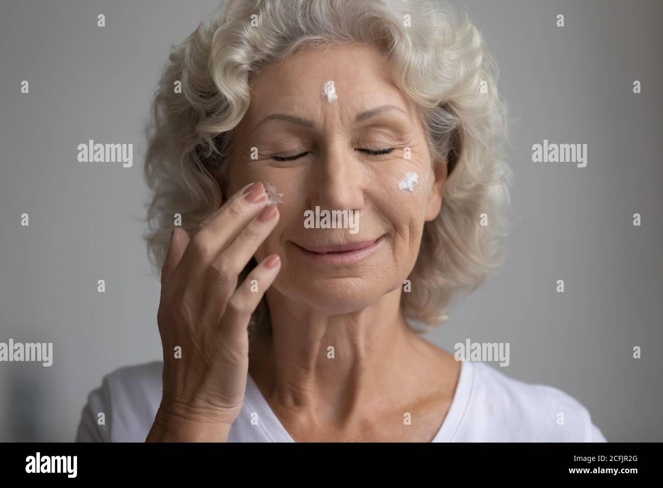 Close up satisfied middle aged woman applying moisturizing face cream Stock Photo