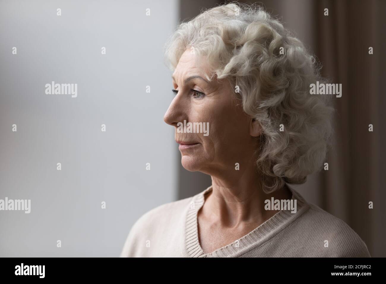 Close up upset thoughtful mature senior woman looking out window Stock Photo