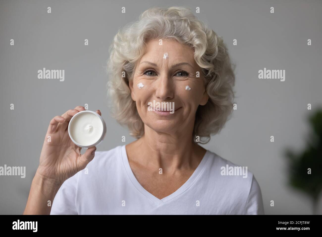 Head shot portrait satisfied mature woman holding moisturizing cream jar Stock Photo