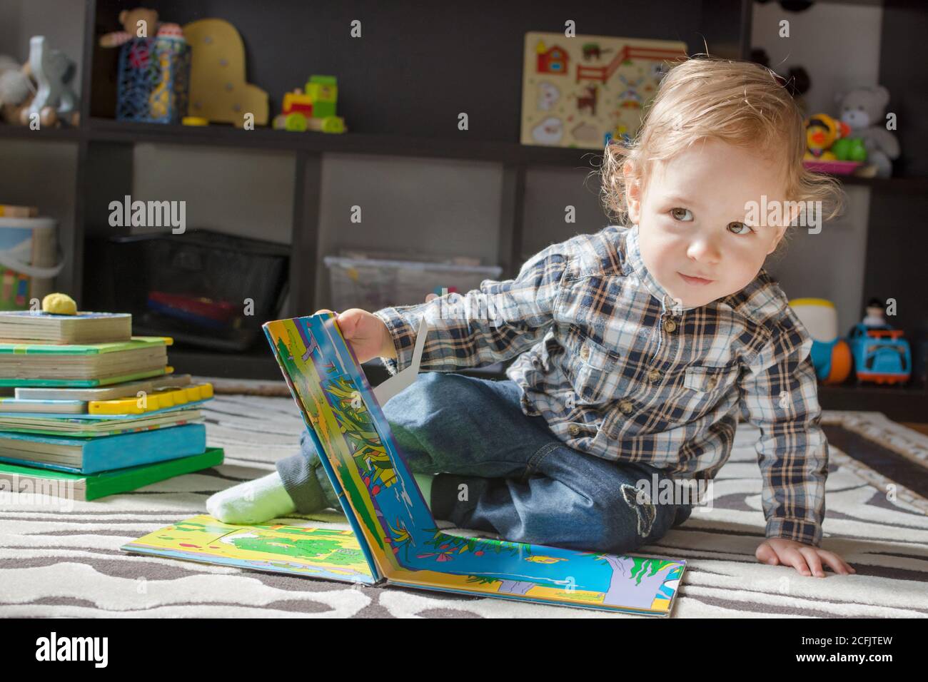Happy sweet baby boy reading books sitting on the floor, at home Stock