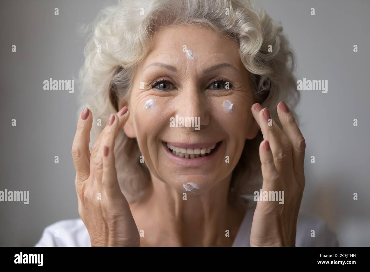 Head shot portrait smiling beautiful mature woman applying cream Stock Photo