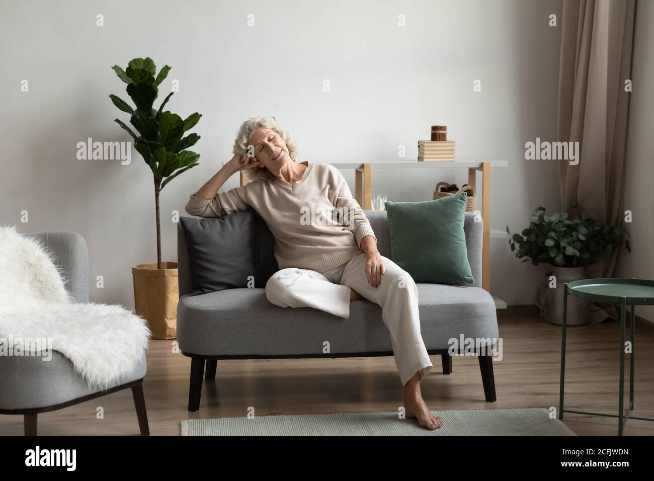 Calm mature woman sitting, relaxing on cozy couch at home Stock Photo