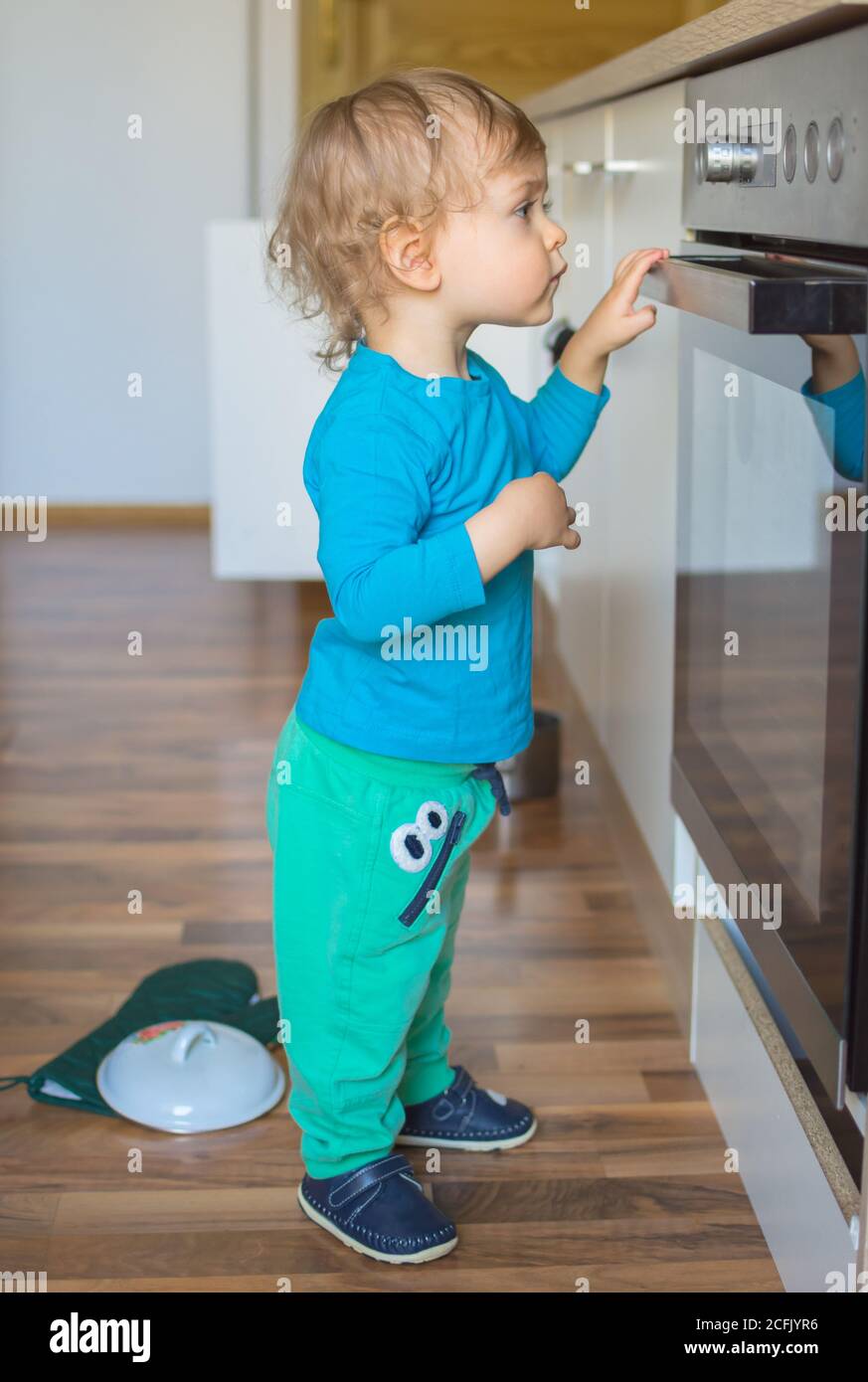 Small and curious child playing with the knobs of the oven in the kitchen. Danger for unattended children, accident prevention at home conceptual phot Stock Photo
