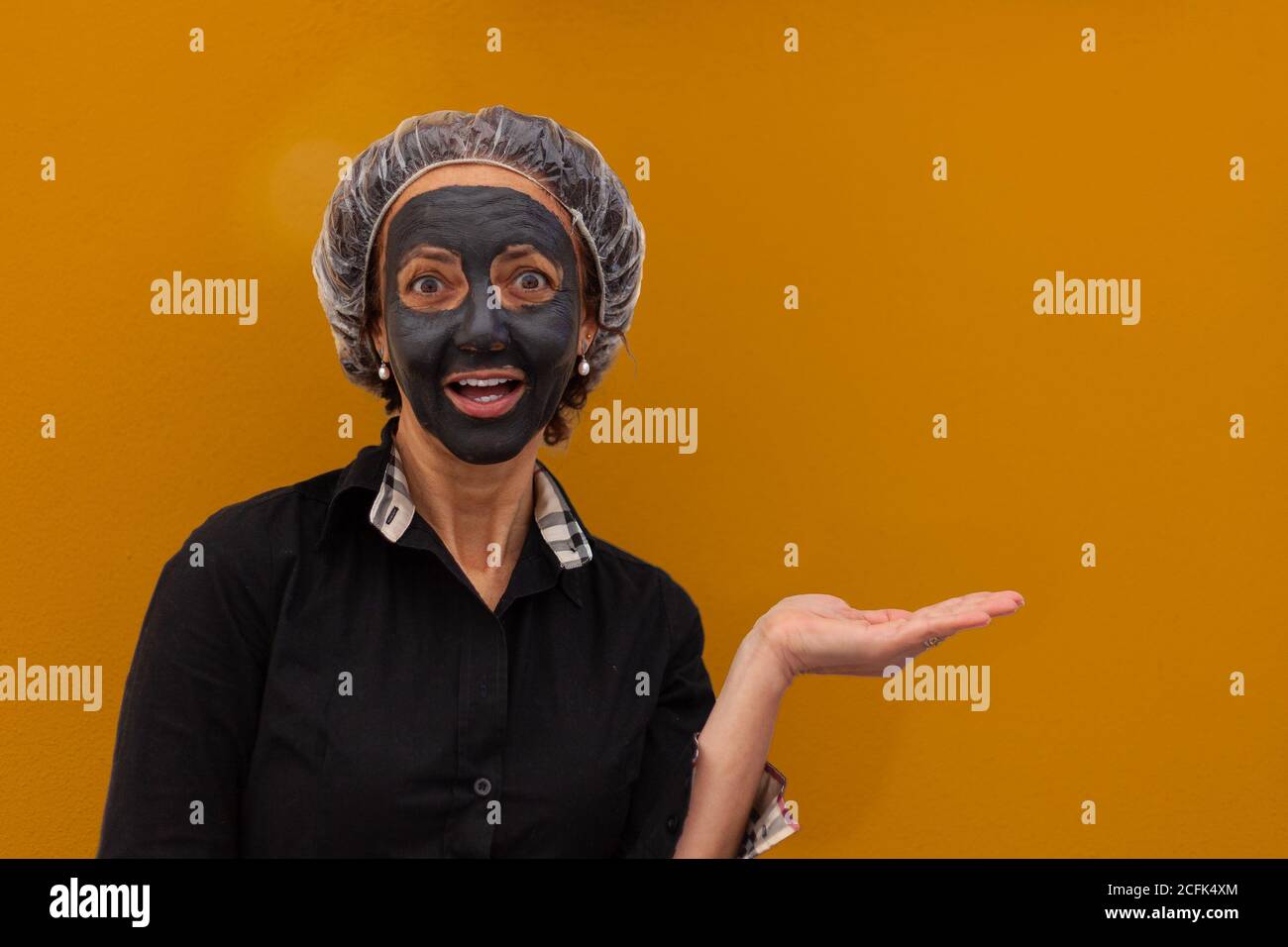 Woman with mud mask and surprised expression showing the palm of her