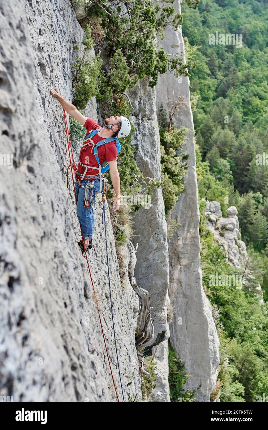 Side view of mountaineer in safety equipment climbing steep rock during