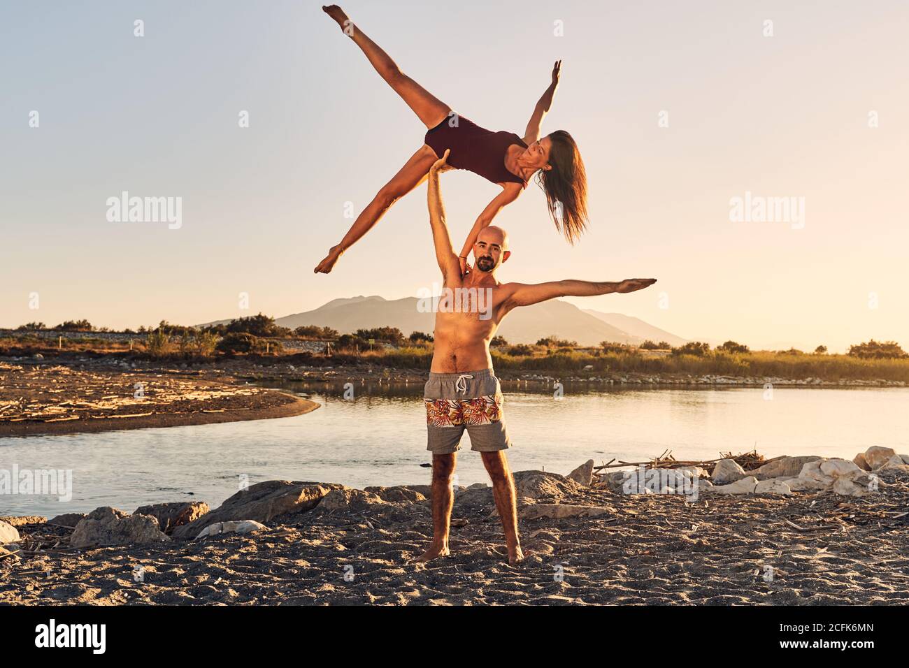 Slim woman leaning on shoulder of man and balancing on arm while doing acroyoga together near river Stock Photo