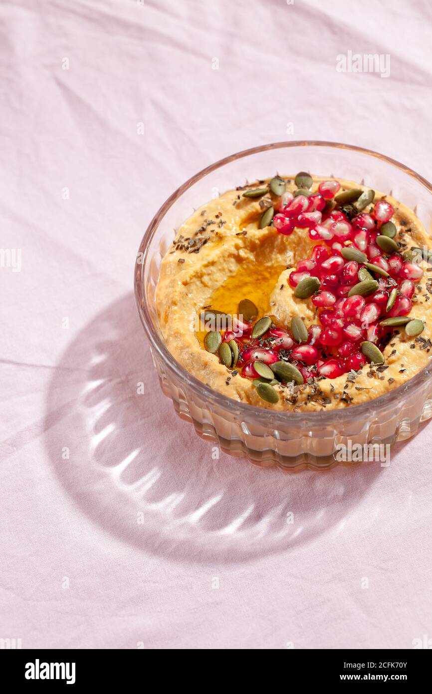 Pumpkin hummus dip with pomegranate and seed topping on pink textile background. Healthy Thanksgiving vegetarian appetizer. Top view Stock Photo
