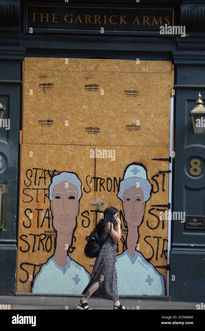 London, UK. 5 September 2020. A women walks past The Garrick Arms Pub in Charing Cross Road remains boarded up, a mural painted with the NHS workers. Stock Photo
