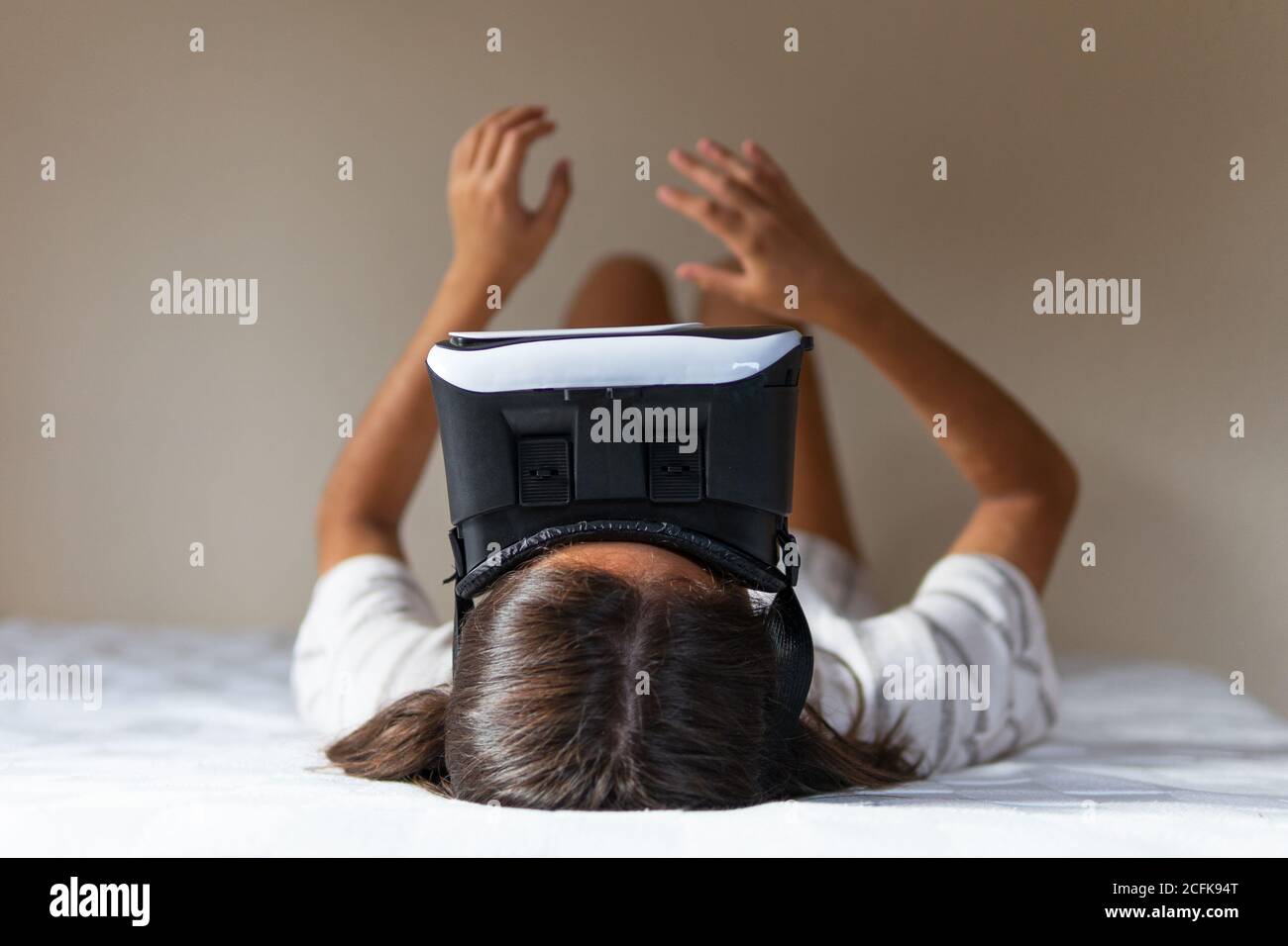 Happy young female in VR headset while lying on bed and exploring cyberspace at home Stock Photo