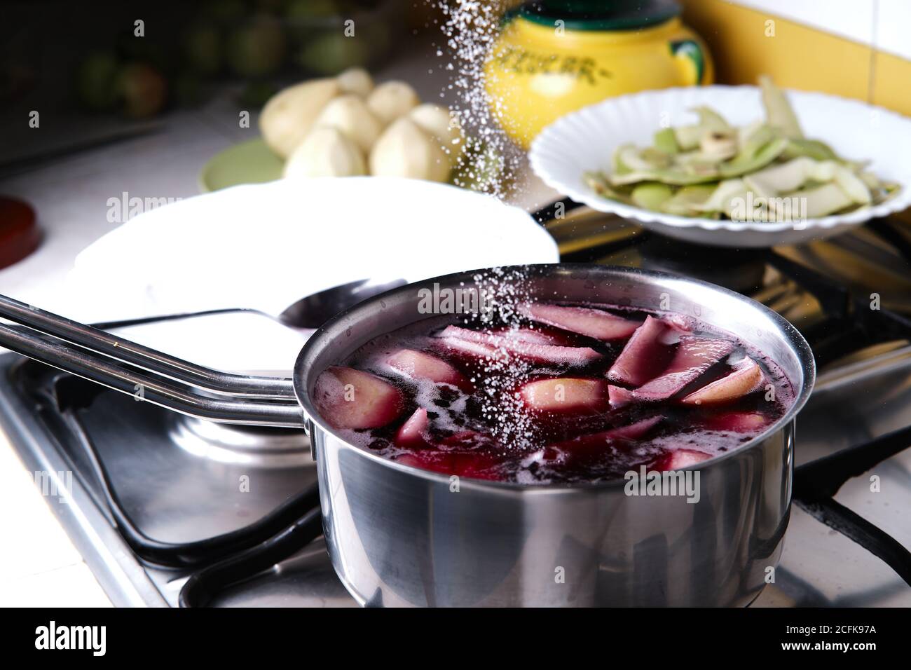 unrecognizable cook adding sugar into saucepan with red wine and pears while preparing delicious  dessert at home Stock Photo