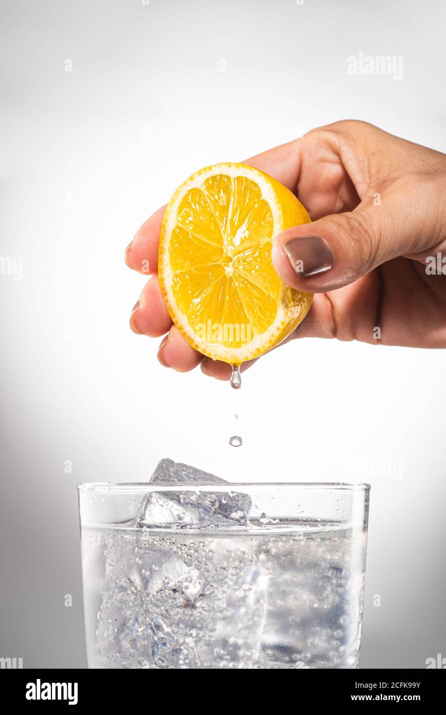 Crop female squeezing lemon juice in glass of water with ice cubes while  preparing detox drink Stock Photo - Alamy