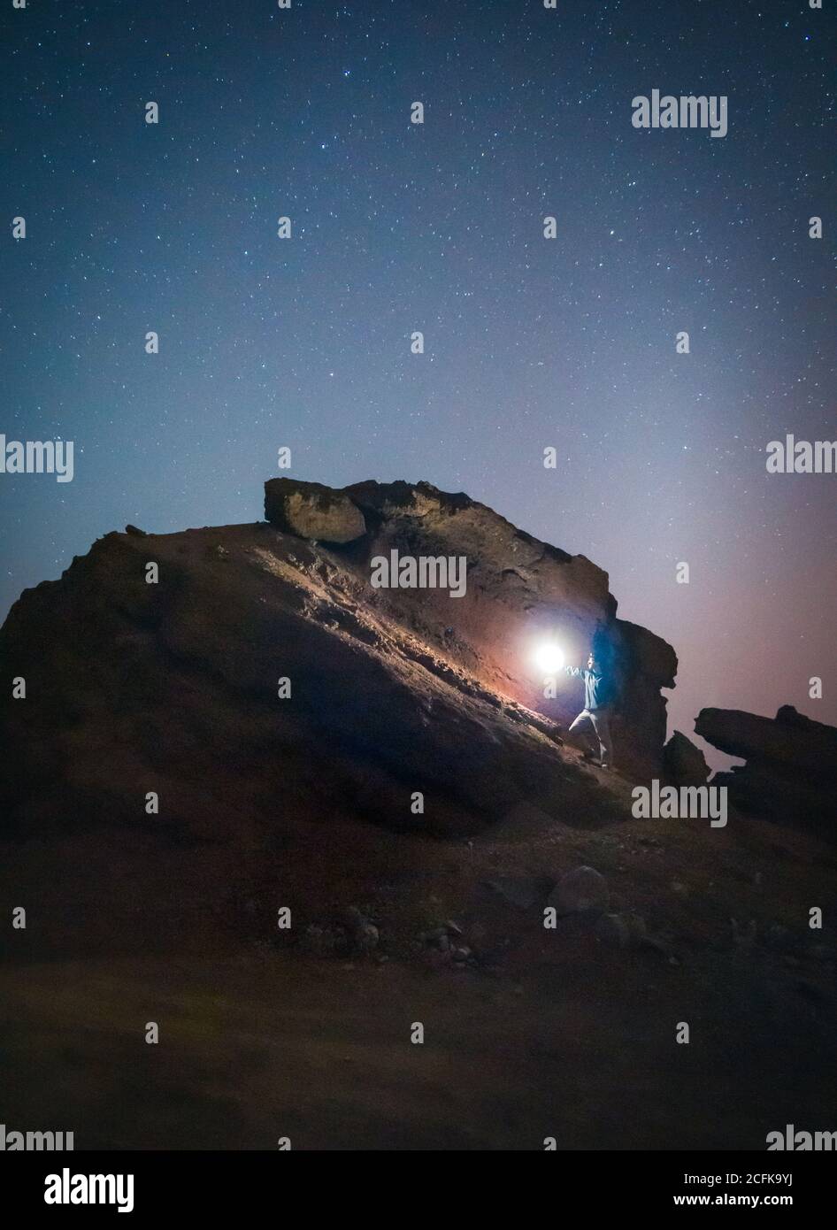 anonymous tourist standing with illuminated torch on stone in mountains on background of starry sky at night Stock Photo