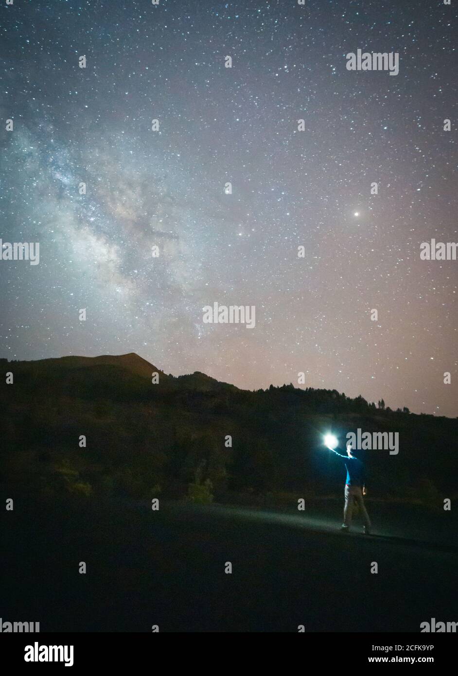 anonymous tourist standing with illuminated torch on empty road in mountains on background of starry sky at night Stock Photo