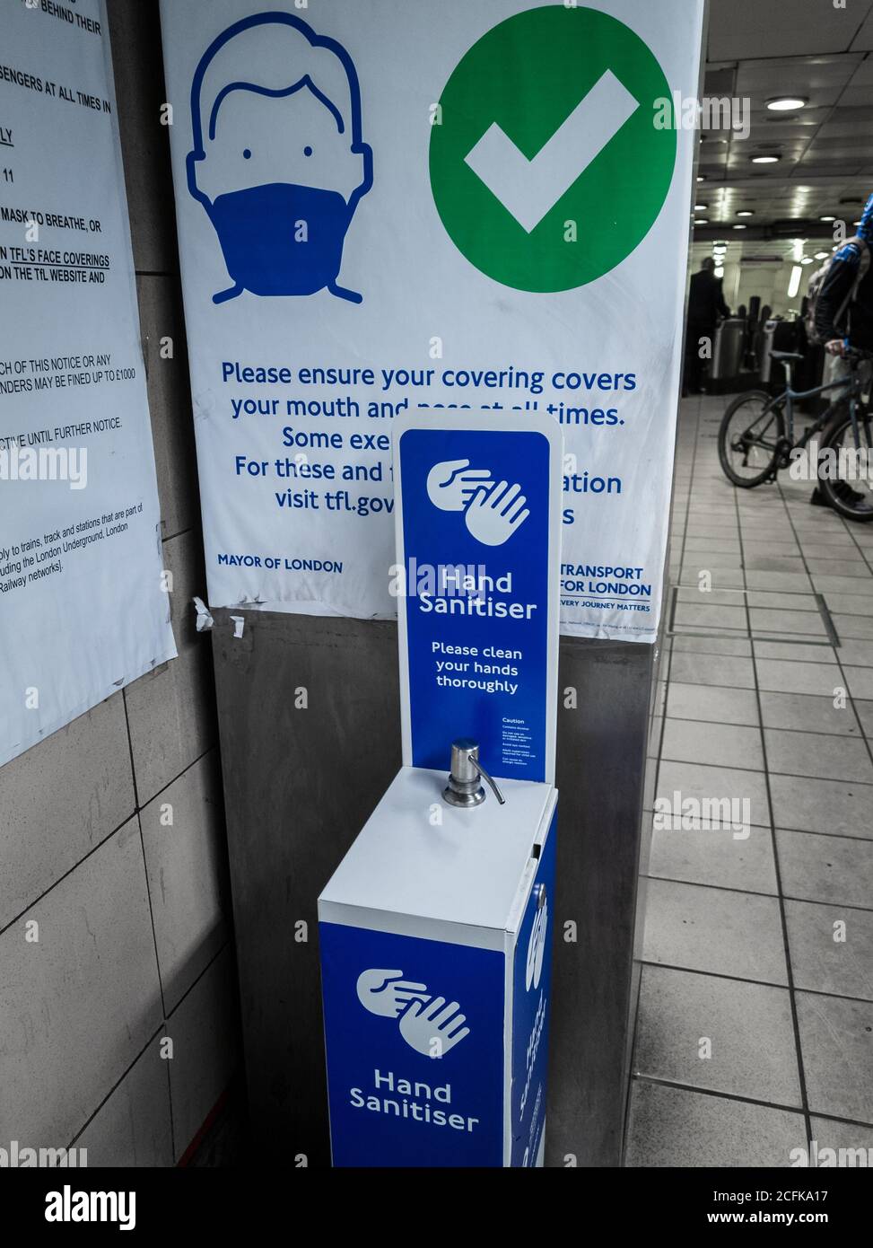 A hand sanitizer station and passenger notice by the entrance of a London Underground station informing people of  Covid-19 travel rules. Stock Photo