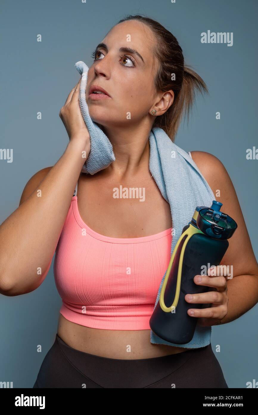 Portrait of a young curvy sporty caucasian woman wiping the sweat from your face with a towel while holding a bottle of water isolated on a with blue Stock Photo