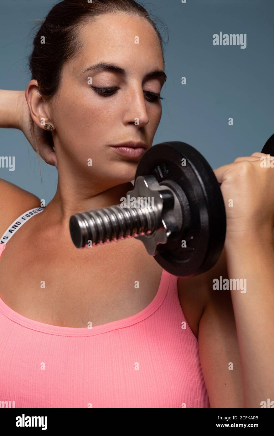 Close up of a young caucasian woman focused on her exercise with a dumbbell isolated on a blue background Stock Photo
