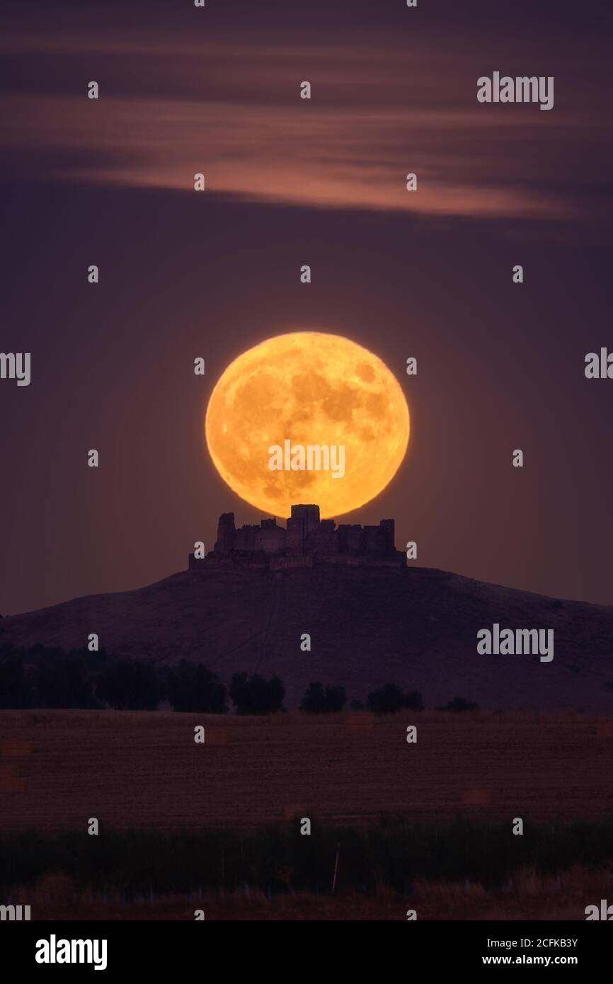 Bright yellow moon glowing on night sky over distant castle and fields in countryside Stock