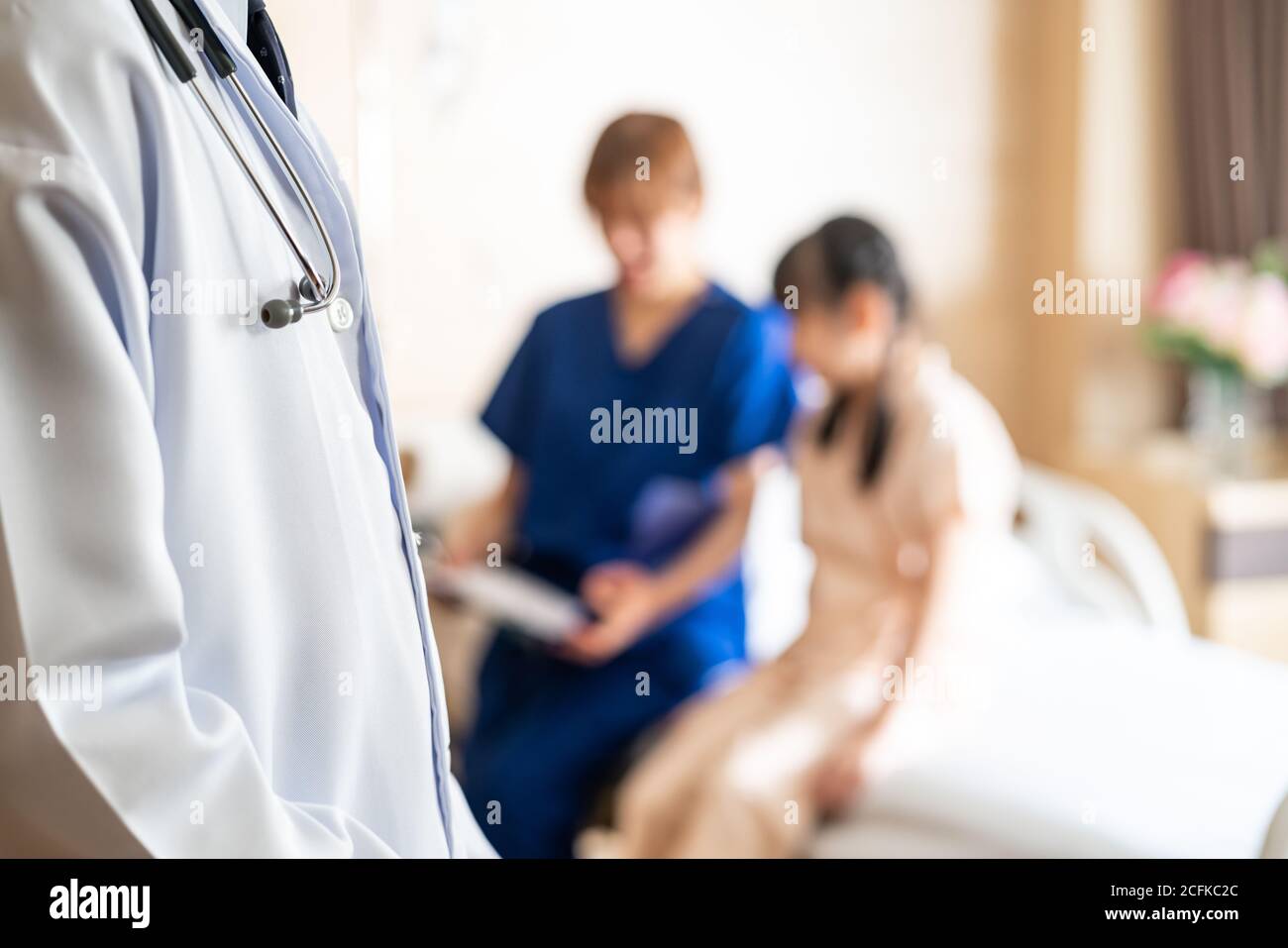 Close up doctor with stethoscope visiting patient in ward with blurred background of nurse taking care of little girl in bed of patient room. Medical Stock Photo