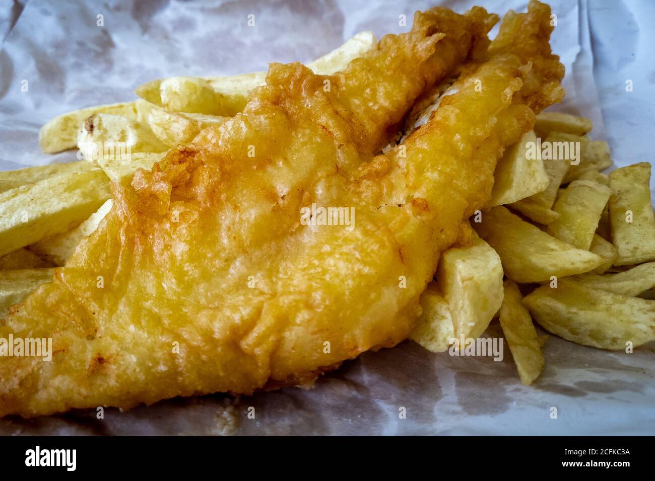 The British cultural cuisine Fish and Chips as served by the chips shop wrapped in paper. Stock Photo