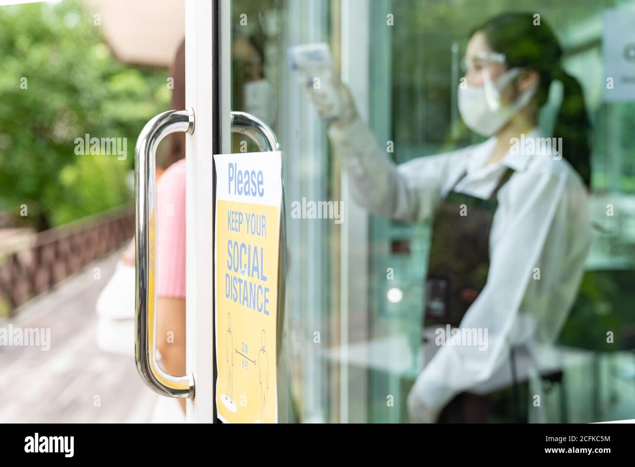 Social distance signage for new normal restaurant with asian waitress taking temperature to customer in background. New normal restaurant lifestyle co Stock Photo