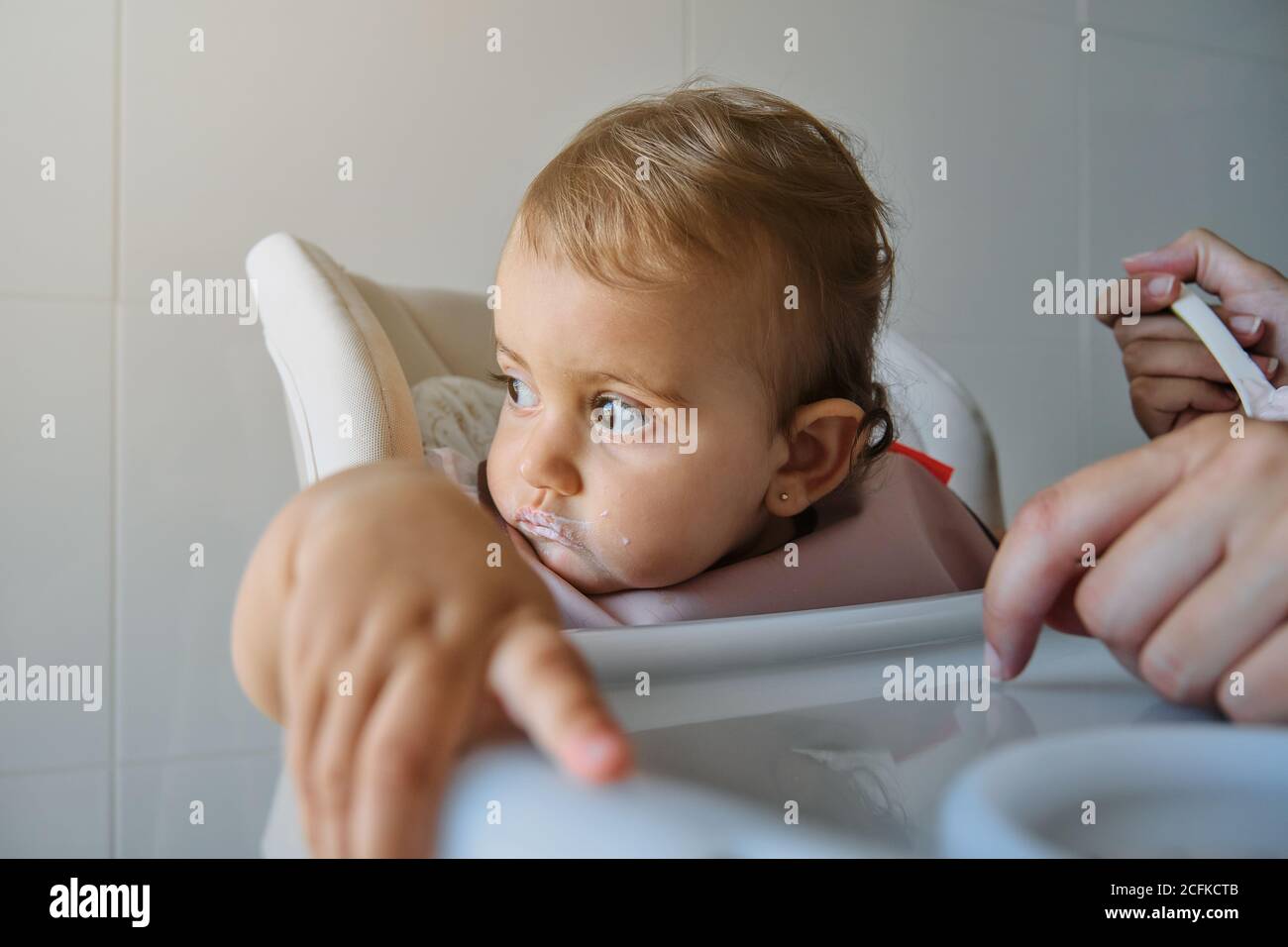 Little girl looking aside distractedly sitting on a high chair with a ...