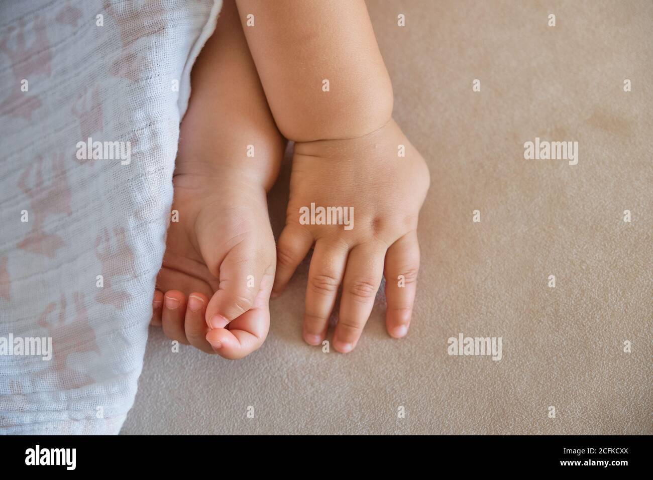 Cropped detail of cute baby's hands covered by a blanket lying on a sofa Stock Photo