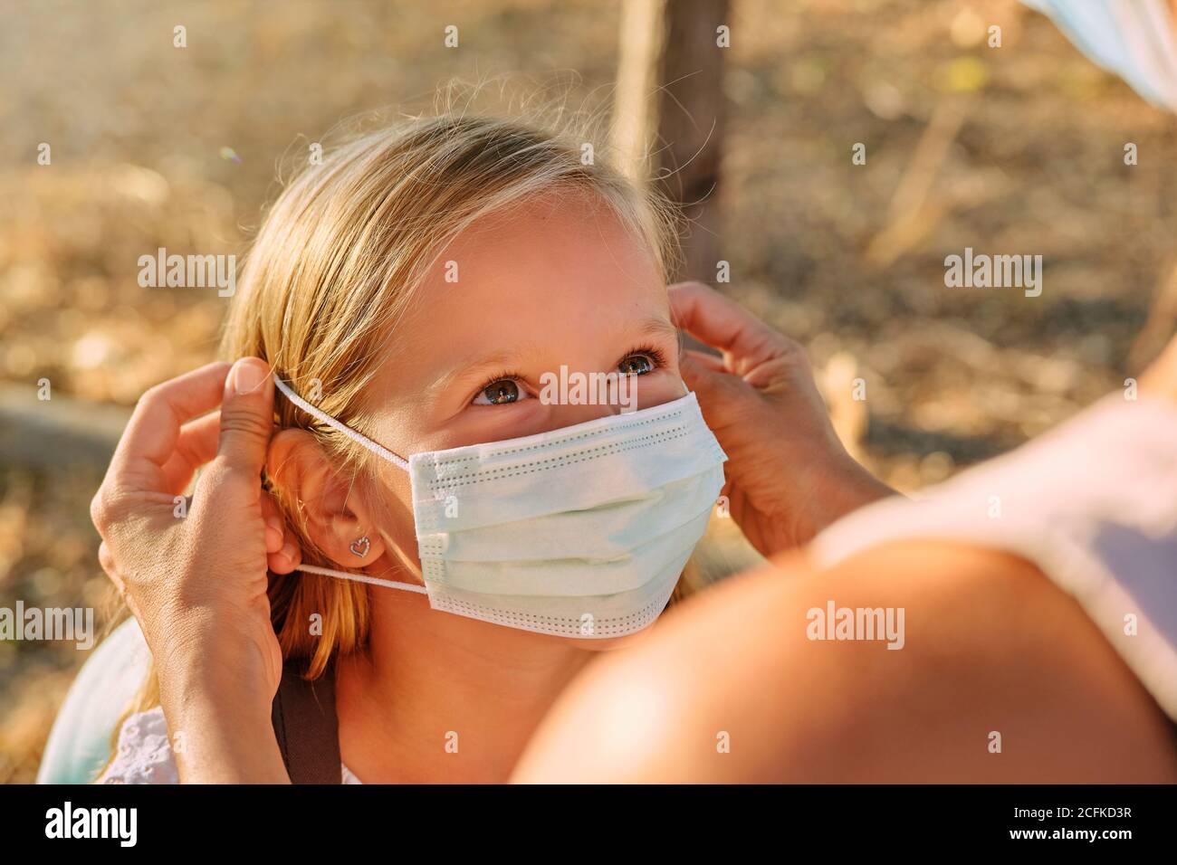 Selective focus on a bright-eyed girl's face while someone puts a mask on her in the middle of a forest Stock Photo