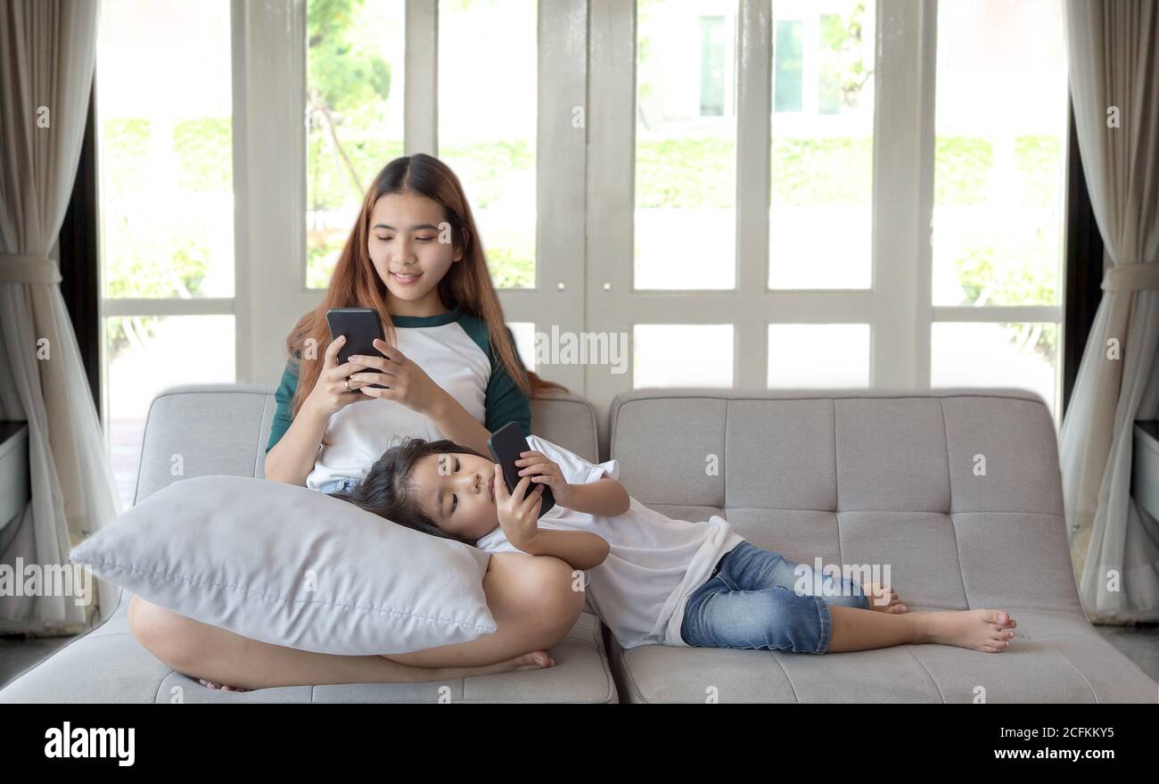 digital generation addict mobile phone concept with asian girl and sister at home Stock Photo