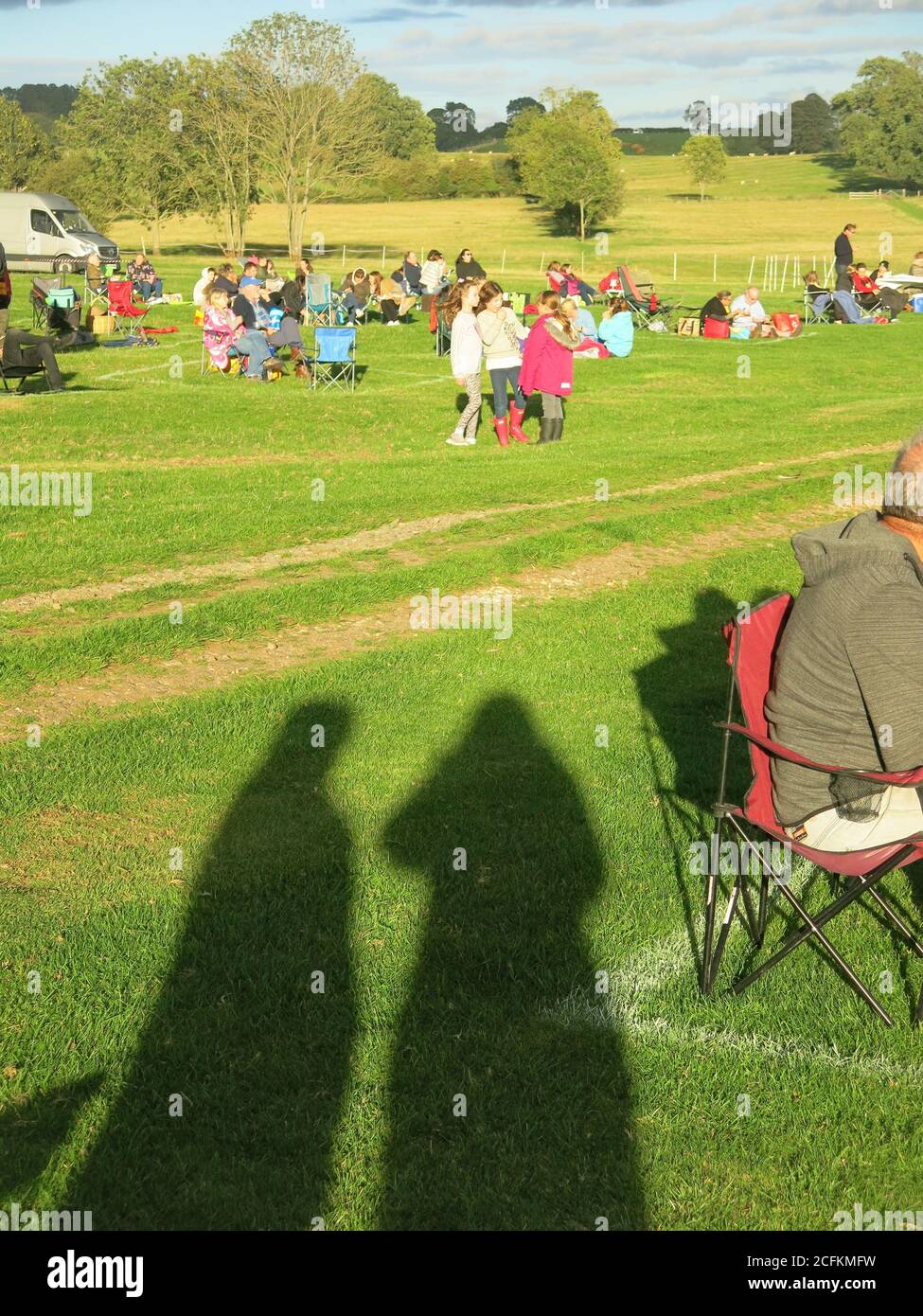 Long shadows of two people cast by the evening sun in a field of picnickers at an outdoor cinema, Winwick Hall, Northamptonshire. Stock Photo
