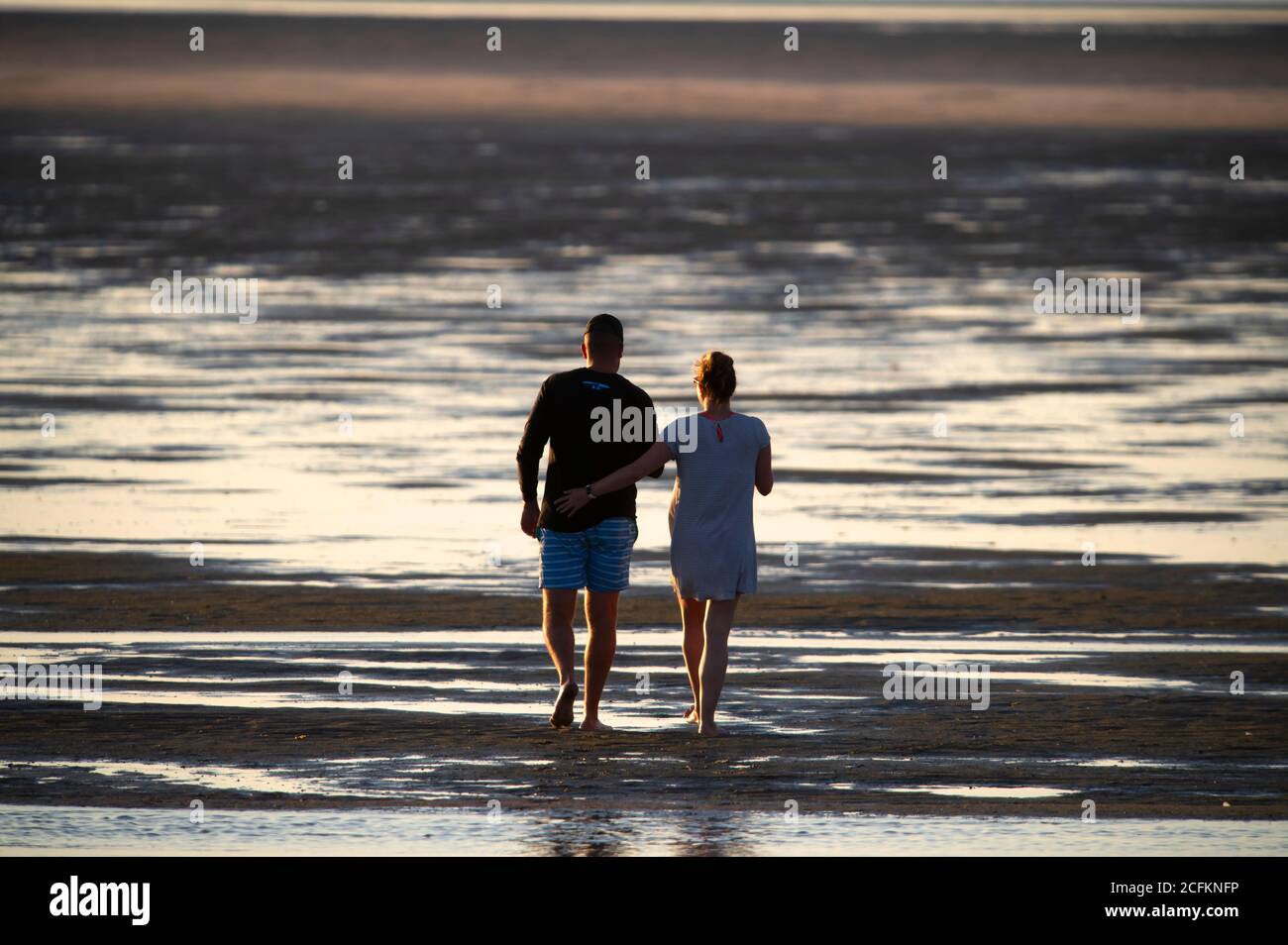 A couple walking along a Cape Cod beach at low tide. Chapin Beach, Dennis, Massachusetts on Cape