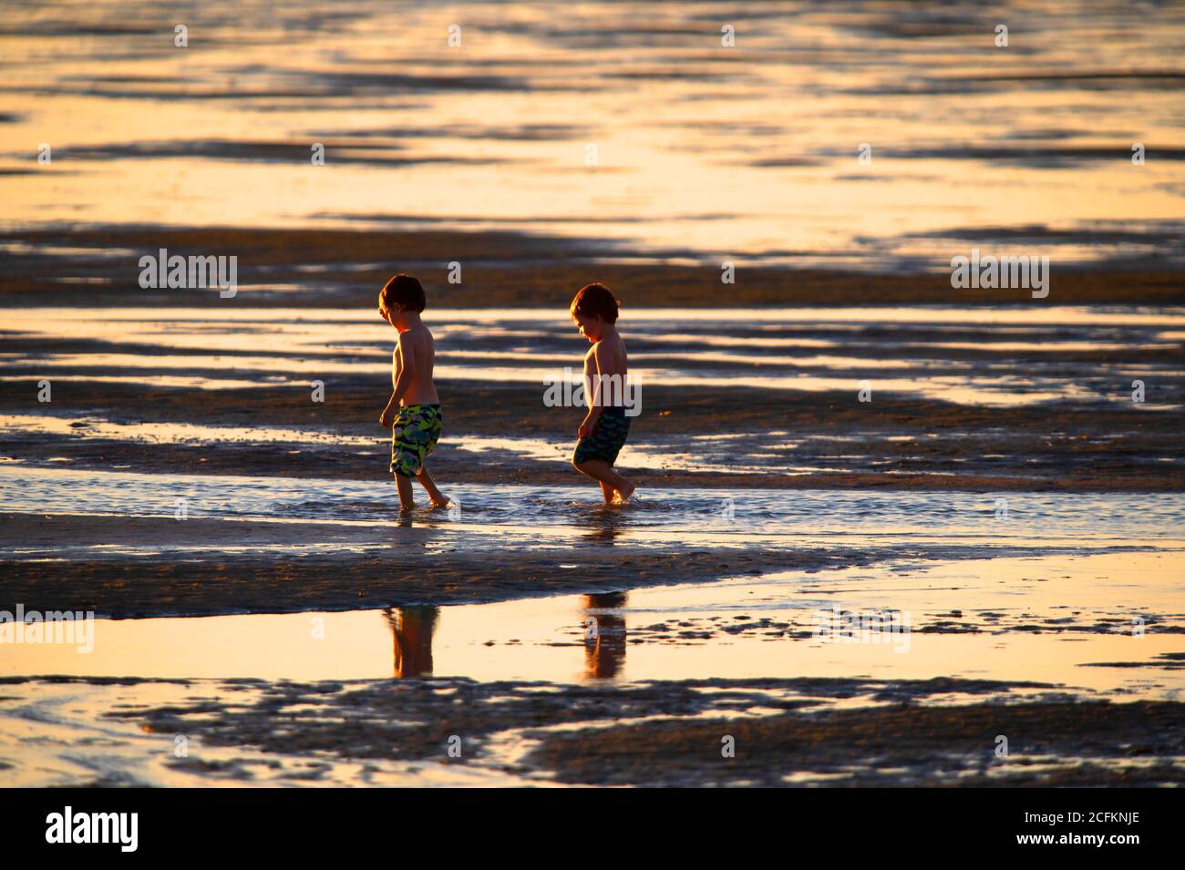 Two boys run along a Cape Cod beach at low tide.  Chapin Beach, Dennis, Mass. USA Stock Photo
