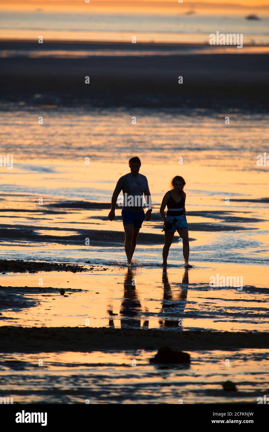 A couple is silhouetted as the walk along a Cape Cod Beach at low tide, Chapin Beach, Dennis, Mass, USA Stock Photo