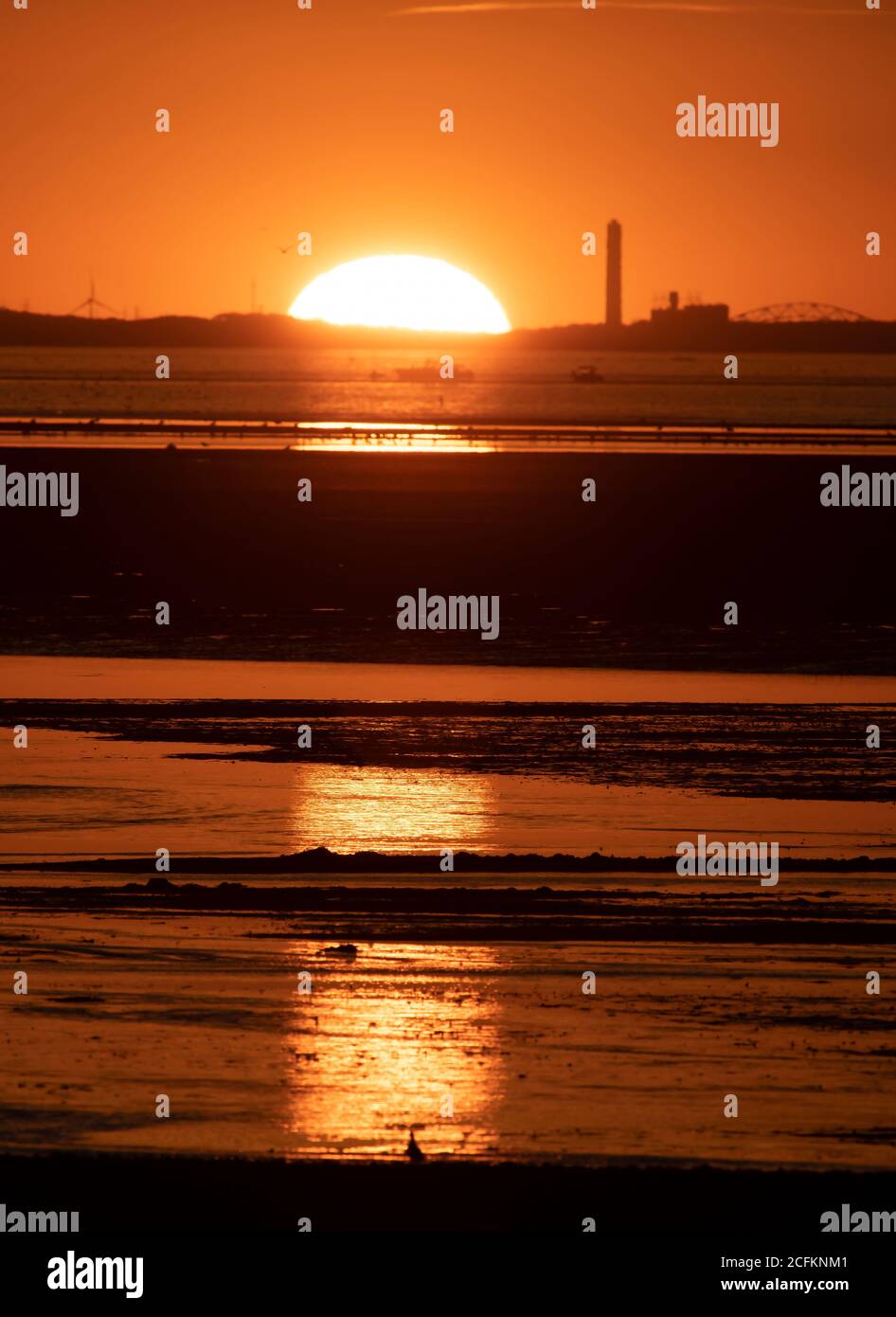 The sun sets behind a power plant on Cape Cod on a summer evening Stock