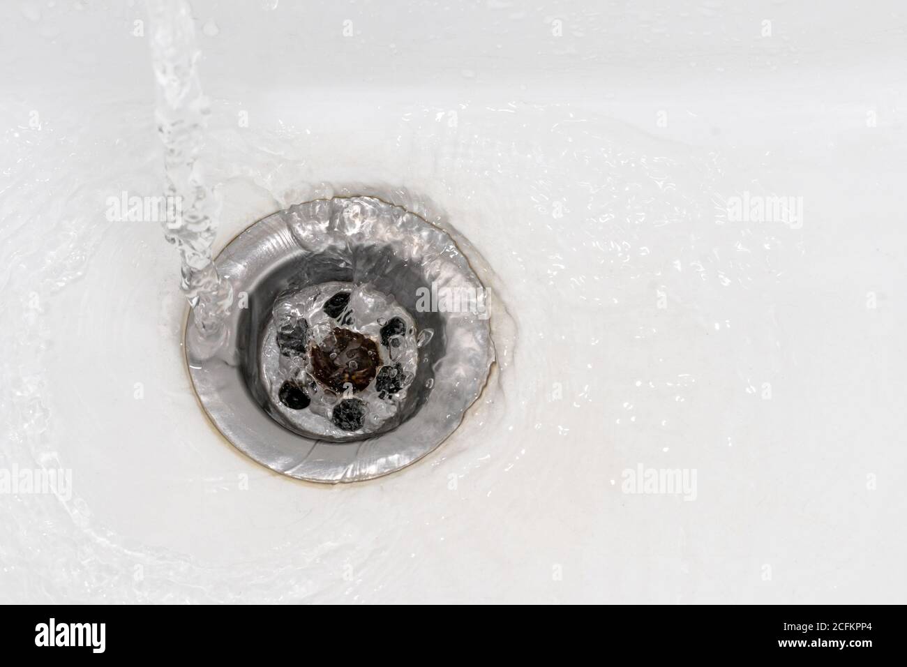 Close up a stream of clean water flows into the sink sewer hole. A jet