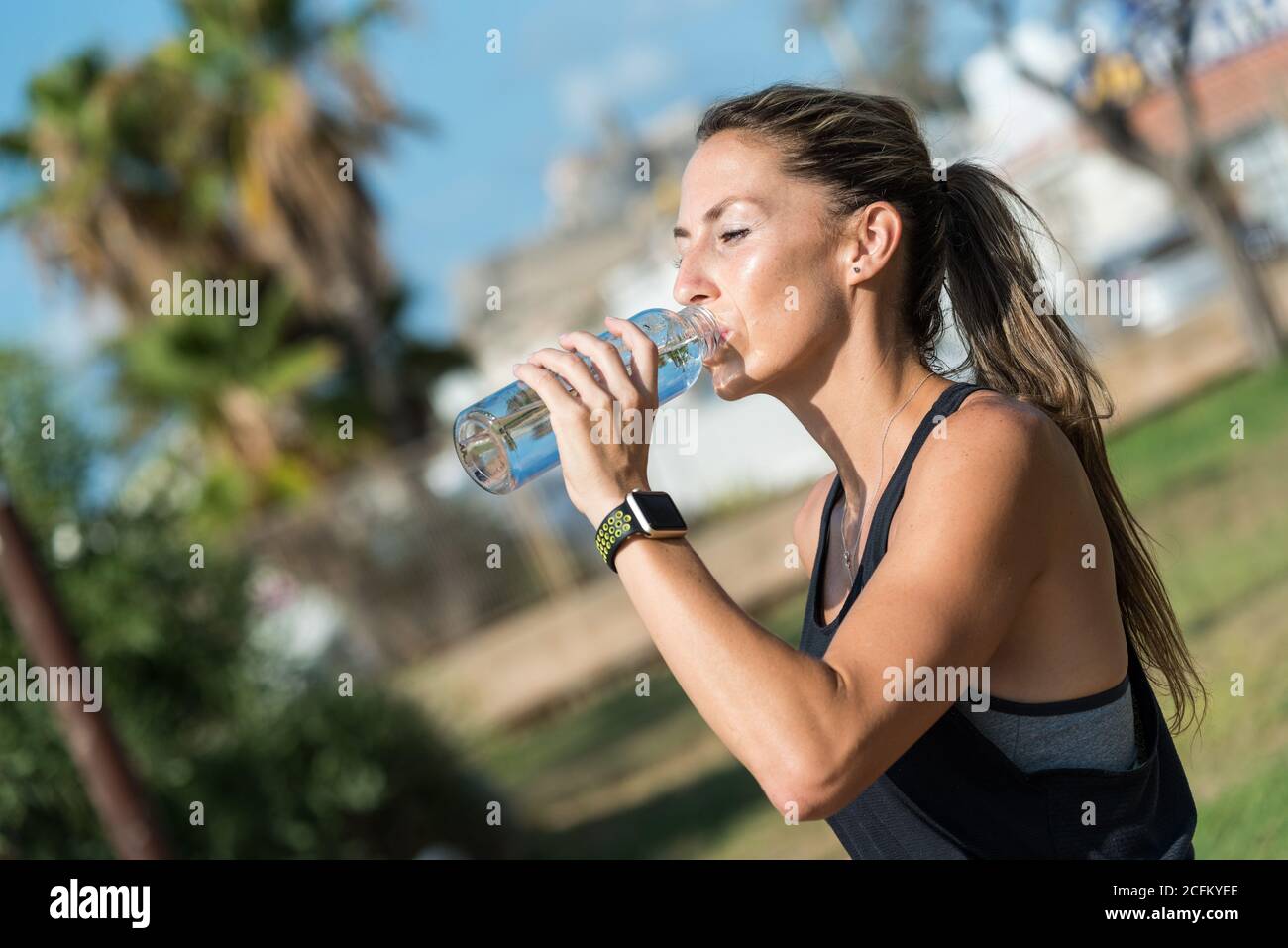 Slim female athlete in sportswear standing drinking water from bottle on sports ground and relaxing during workout on sunny day Stock Photo
