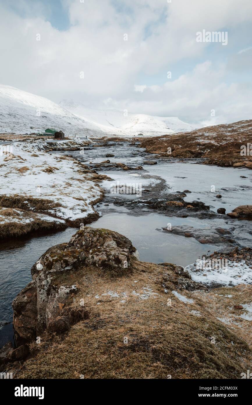 Spectacular scenery of river surrounded by mountain range covered with snow in winter on overcast day on Faroe Islands Stock Photo