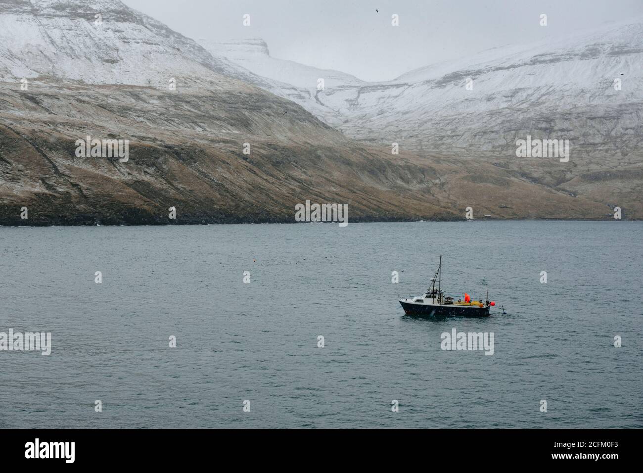 Fish boat on the sea near snowy mountain range during winter on faroe island Stock Photo