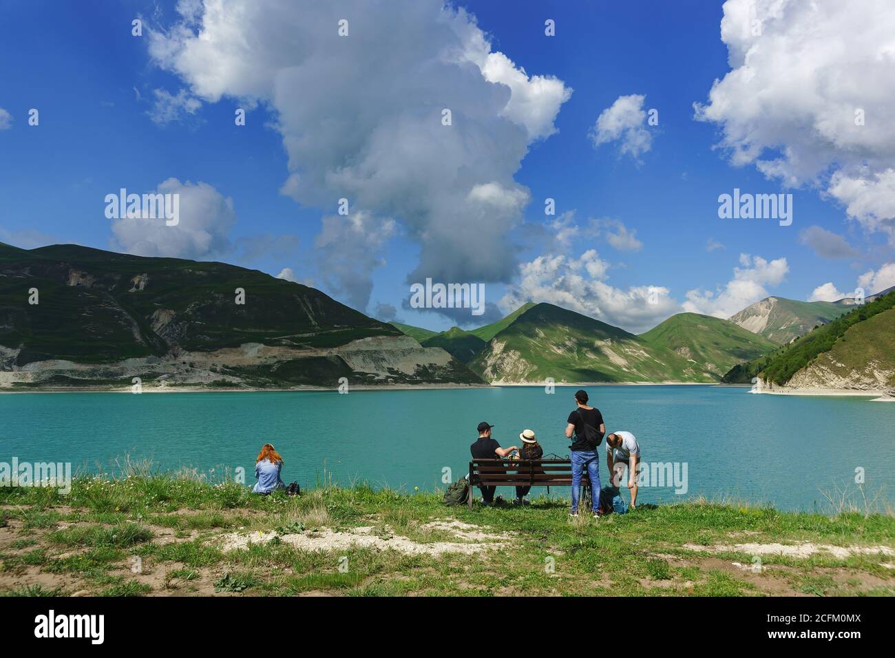 Vedensky district, Chechen Republic, Russia - June 01, 2019: Tourists sit on a bench on the shore of lake Kezenoi am. Green grass on the mountain slop Stock Photo