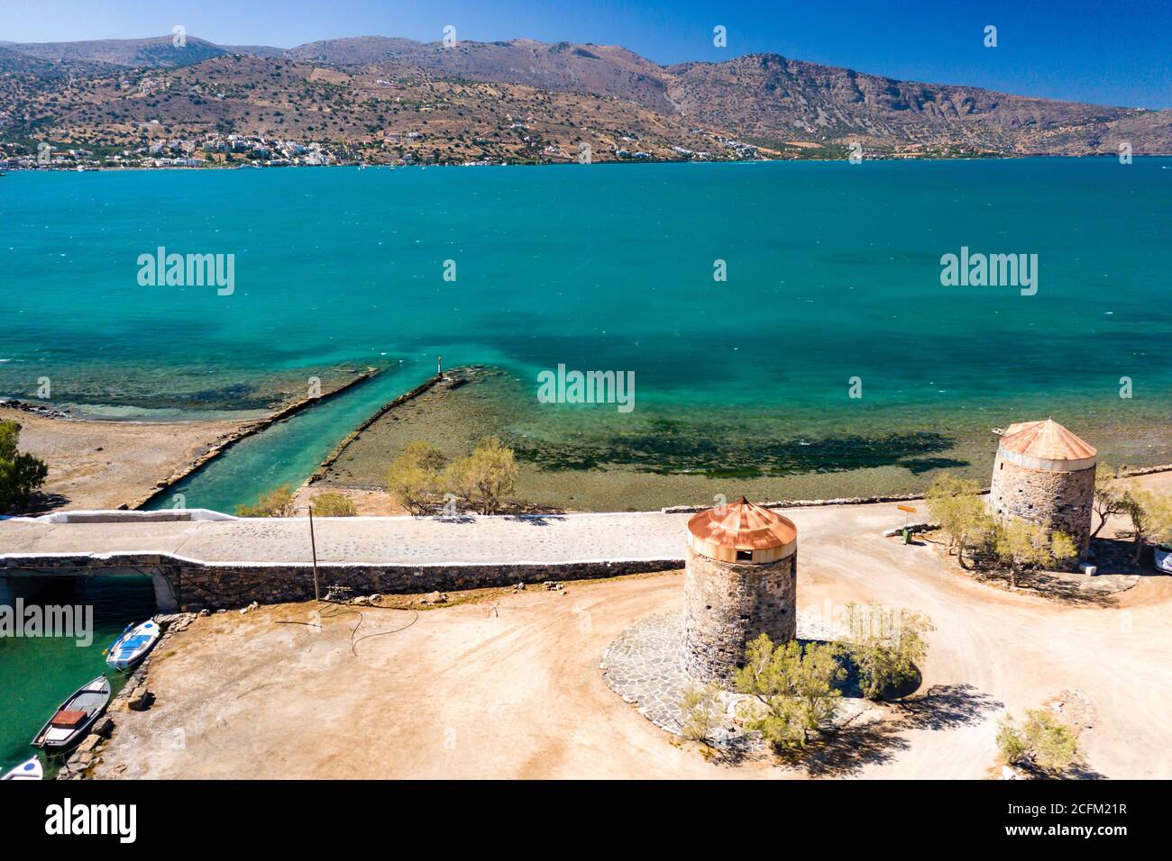 Old windmills and canal on a narrow causeway and site of an ancient Minoan city (Elounda, Crete, Greece) Stock Photo