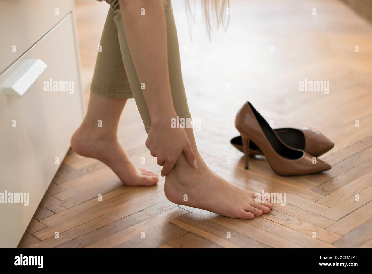Tired woman touching her ankle, suffering from leg pain because of uncomfortable shoes, feet pain wear high heel shoes after work or walk. Swelling of Stock Photo