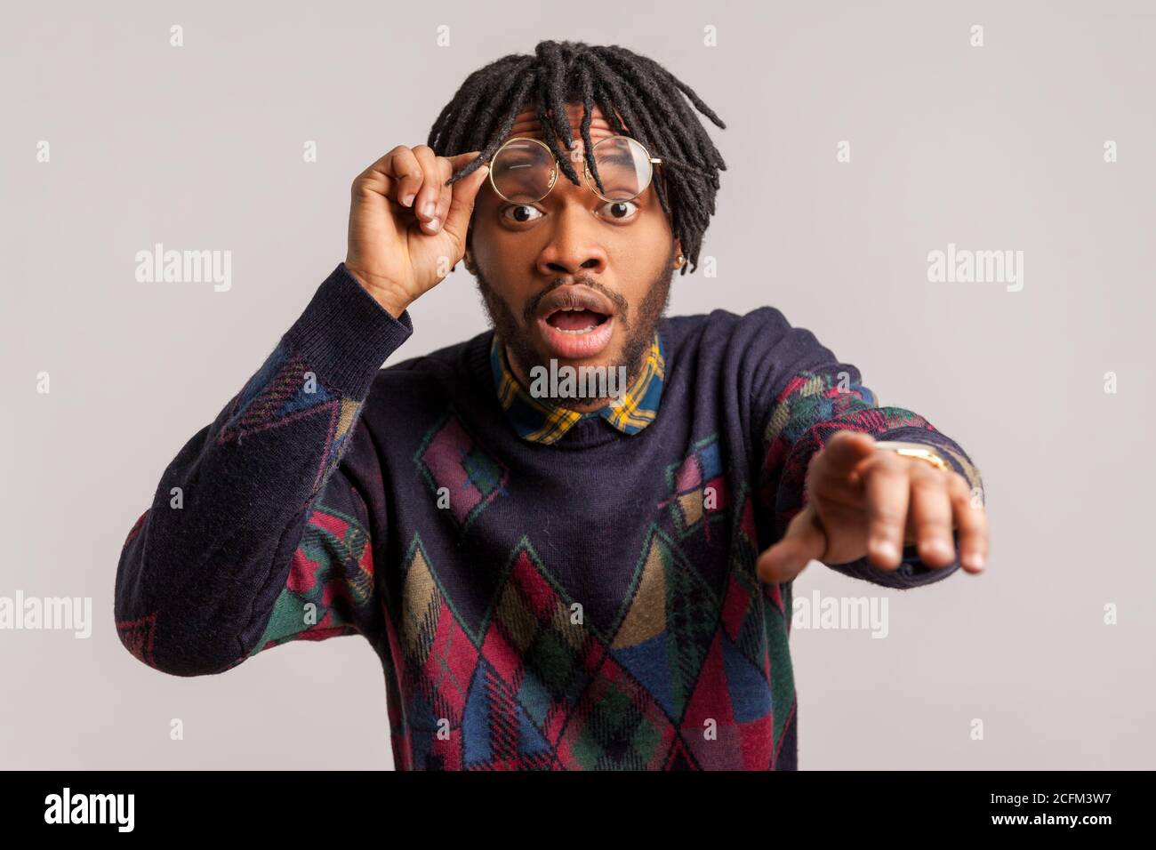 Closeup surprised shocked african man with dreadlocks putting off glasses looking with big eyes and pointing finger at camera, suspecting you. Indoor Stock Photo