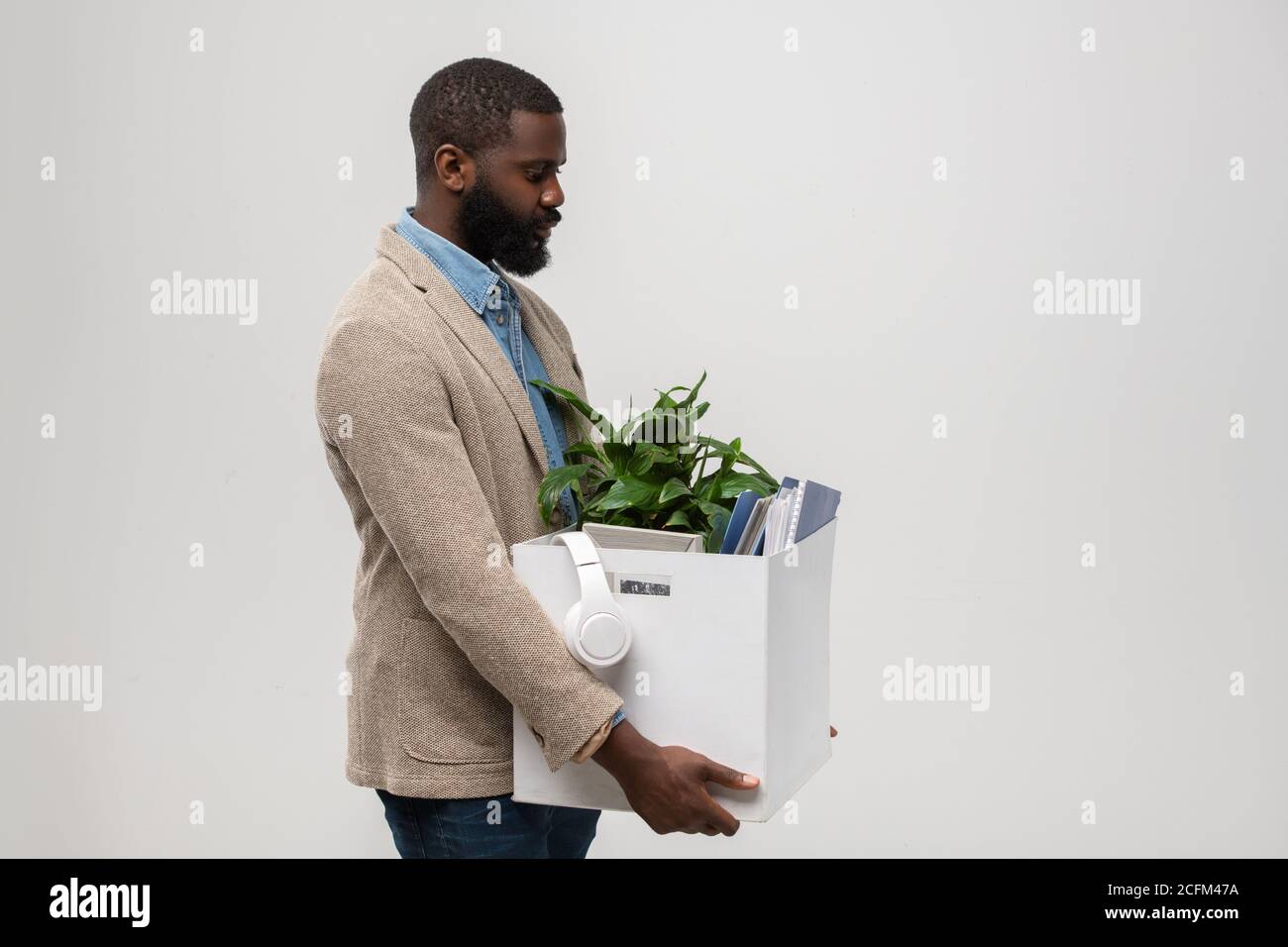 Side view of bearded African-american office manager holding box with supplies Stock Photo