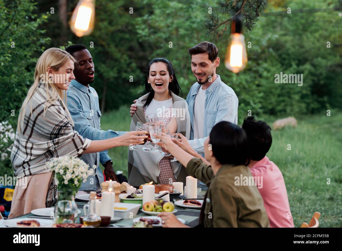 Three happy young restful couples sitting by served table in natural environment Stock Photo