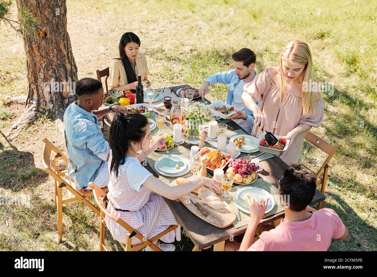 Young blond female in casual dress taking some cooked vegetables from bowl Stock Photo